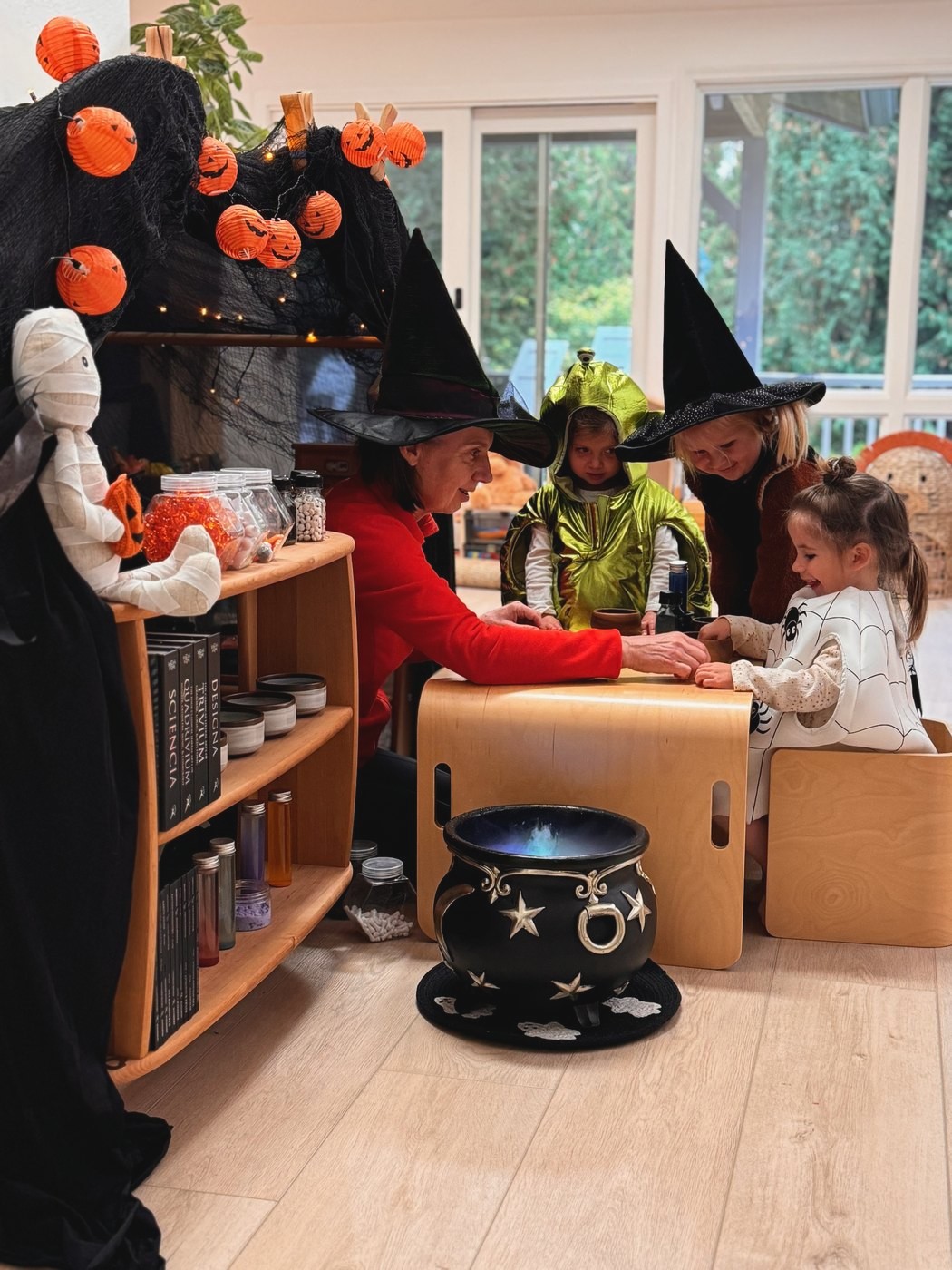 A teacher and children in costumes gathered around a Halloween cauldron activity