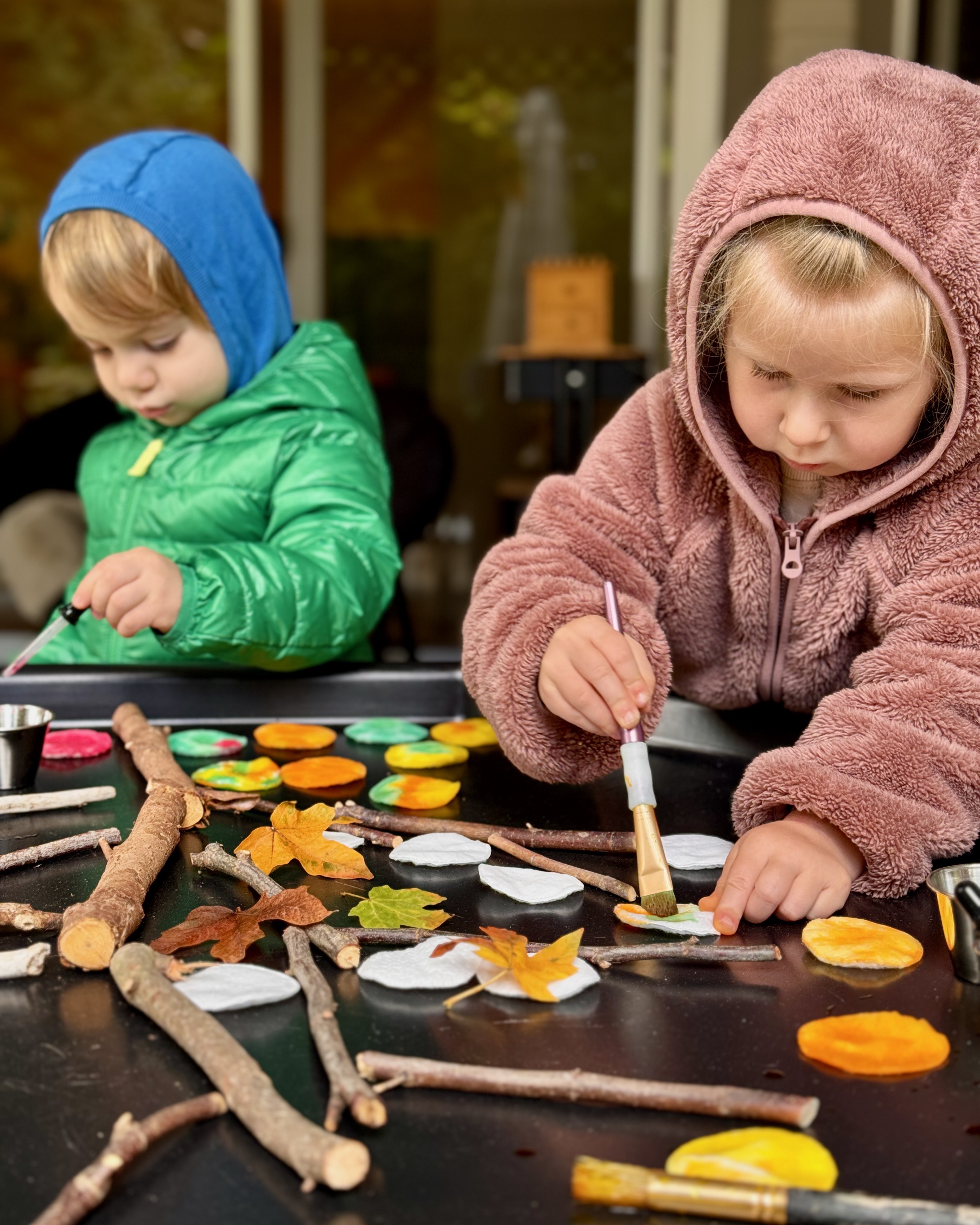 Children creating autumn art with paint and natural materials