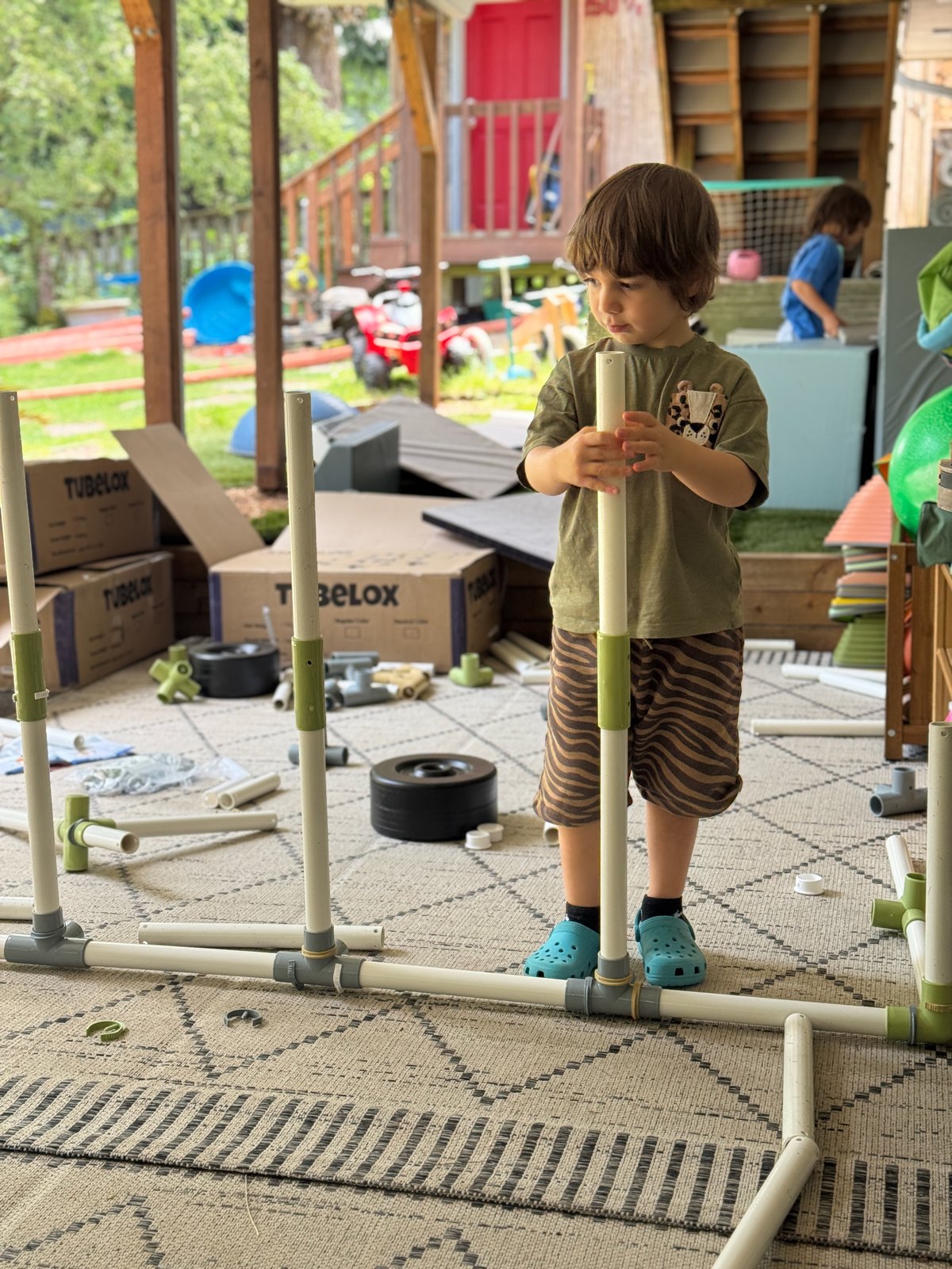 Child building a large structure with tubes and connectors outdoors