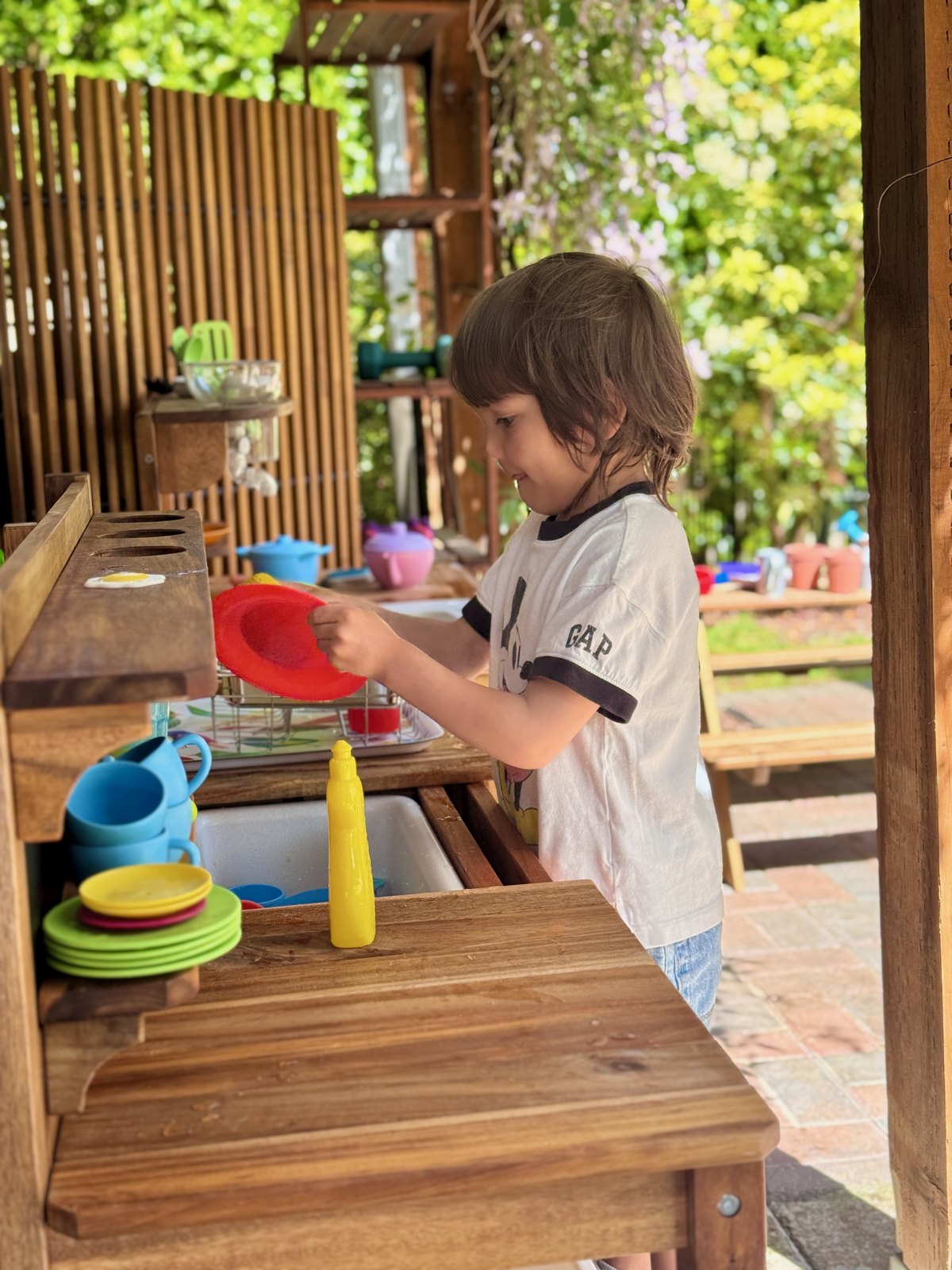 Child washing dishes independently in the outdoor play kitchen
